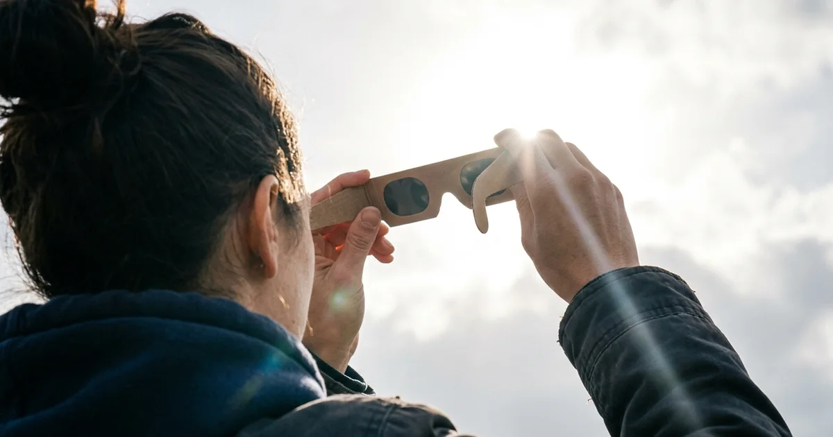 Person wearing certified eclipse glasses looking up at a partially eclipsed sun